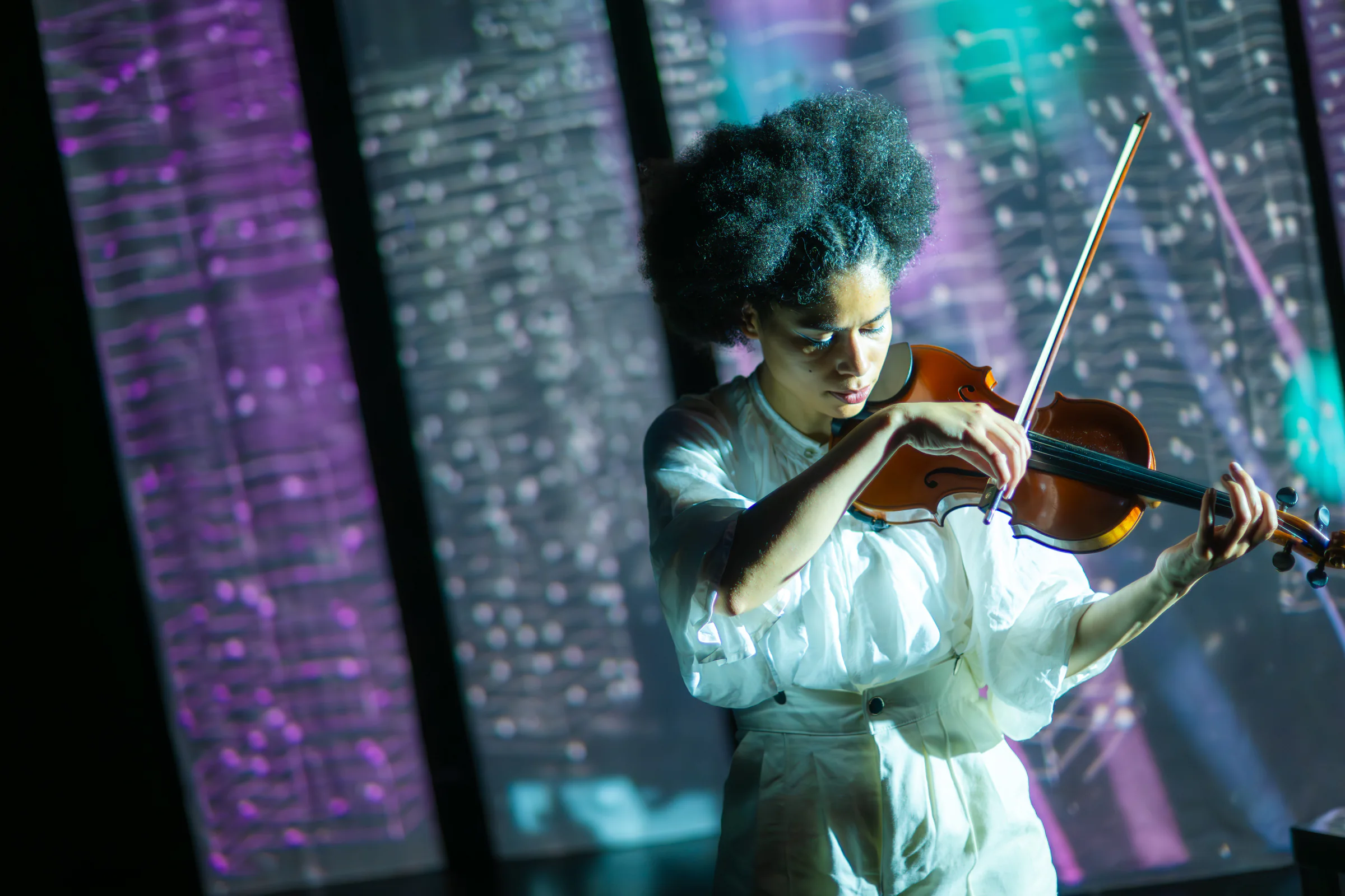 Fay Guiffo plays violin on stage amid projected handwritten music.