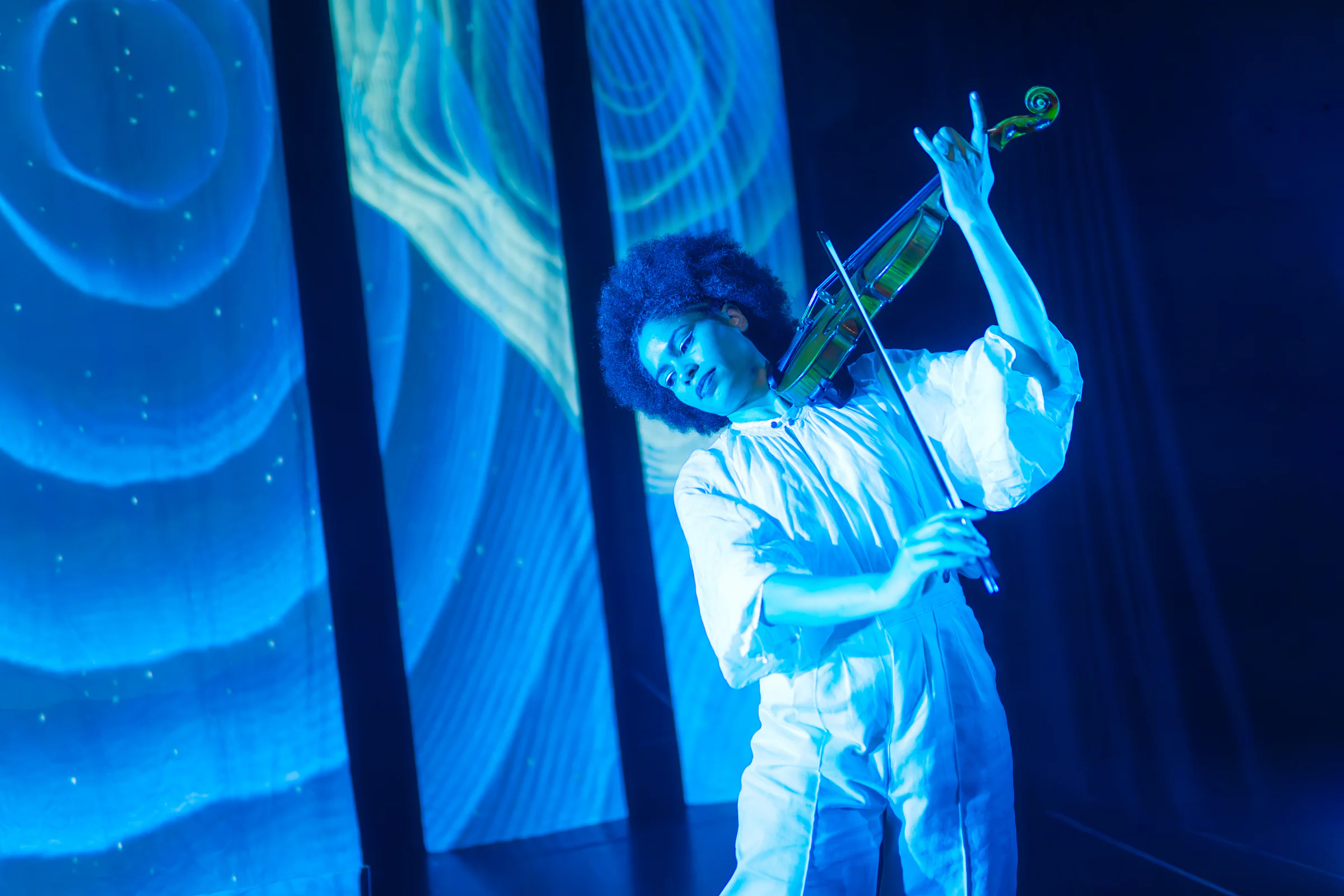 Fay Guiffo plays violin beneath flowing blue projected lines.